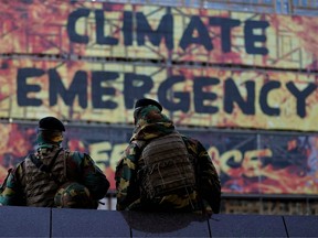 Two soldiers look at a group of activist of the environmental NGO Greenpeace taking part in a protest action after attaching a banner on the frontage of the European Council's building, in Brussels, on December 12, 2019 ahead of the European Summit.