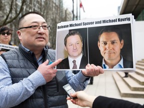 This file picture taken on March 6, 2019 shows Louis Huang of Vancouver Freedom and Democracy for China holding photos of Canadians Michael Spavor and Michael Kovrig, who are being detained by China, outside British Columbia Supreme Court, in Vancouver, as Huawei Chief Financial Officer Meng Wanzhou appears in court.