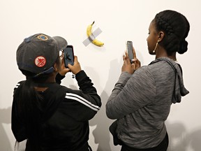 People attending the Art Basel Miami show on Dec. 6, 2019, take a photo of artist Maurizio Cattelan's "Comedian" — a  banana taped to the wall — which was purchased for $120,000.