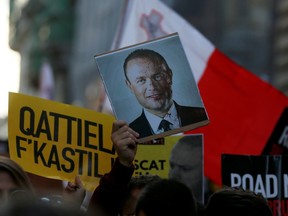 A protester holds a picture of Maltese Prime Minister Joseph Muscat with his face covered in blood, next to a person holding a sign during a demonstration demanding justice over the murder of journalist Daphne Caruana Galizia outside the Parliament House, in Valletta, Malta, December 1, 2019. The sign reads, 'Murderers in Castille.'