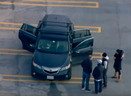 A screenshot of aerial footage showing authorities, on the top level of the parkade, gathered around the black vehicle with three of its doors left open. The woman and two children were found dead on the pavement below. 