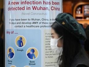 A woman passes a sign warning passengers arriving on flights into the U.K. about the coronavirus, London Heathrow Airport on Jan. 28, 2020.