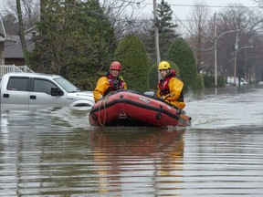 Firefighters make their way through a flooded street on Friday, May 3, 2019 in Ste-Marthe-sur-la-Lac, Quebec. A federal review says the government had trouble spending half of the $184 million earmarked to prevent flood damage in Canadian communities.
