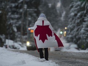 A man wearing a Canadian flag stands in the middle of a snow-covered road while he waits for the bus in North Vancouver, B.C., Wednesday, January 15, 2020. Vancouver and the lower mainland have been hit with cold temperatures and snow.