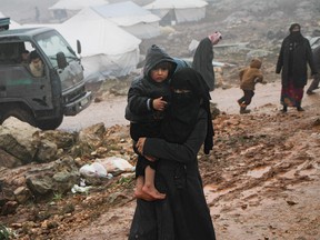 A Syrian woman, who fled from government forces' advance on Maaret al-Numan in the south of Syria's Idlib province, carries a child at a camp for displaced people near the village of Harbnoush on Dec. 27, 2019.