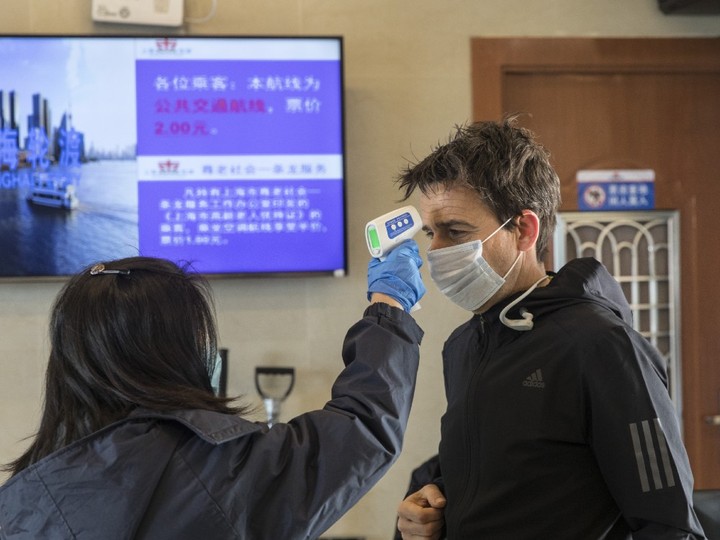  A transit worker takes the temperature of a passenger during a screening at a passenger ferry terminal in Shanghai, China, on Thursday, Jan. 30, 2020.