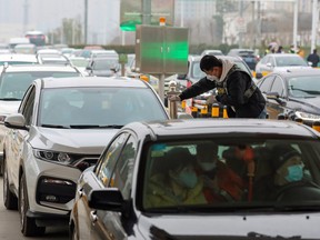 A sanitation and epidemic prevention team worker checks the body temperature of a passenger in a car at a toll station in Wuhan, China, Jan. 23, 2020.