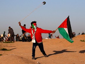 A young Palestinian protester, wearing a Guy Fawkes mask painted in the colours of the Palestinian flag and holding a Palestinian flag in his hand, uses a slingshot to hurl objects during clashes following a demonstration near the border with Israel east of Gaza City on Jan. 4, 2019.