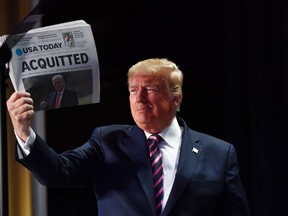 US President Donald Trump holds up a newspaper that displays a headline "Acquitted"  as he arrives to speak at the 68th annual National Prayer Breakfast on February 6, 2020 in Washington,DC.