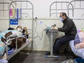 This photo taken on February 17, 2020 shows a man (R) who has displayed mild symptoms of the COVID-19 coronavirus using a laptop at an exhibition centre converted into a hospital in Wuhan in China's central Hubei province.