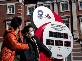 A couple wearing protective face masks, following an outbreak of the coronavirus, walk past the big Omega One-Year Countdown clock for the opening ceremony of the Tokyo 2020 Olympic outside of Tokyo Station in Tokyo, Japan, February 27, 2020.