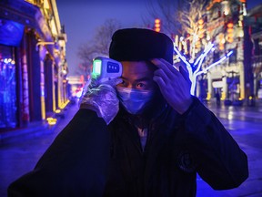 A Chinese worker wears a protective mask as he has his temperature checked in a nearly empty and shuttered commercial street on Feb. 12, 2020 in Beijing, China.