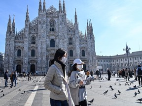 Two women wearing a protective facemask walk across the Piazza del Duomo, in front of the Duomo, in central Milan, on February 24, 2020 following security measures taken in northern Italty against the COVID-19 the novel coronavirus.