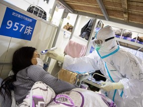 A woman displaying mild symptoms of the COVID-19 coronavirus has her temperature checked at an exhibition centre converted into a hospital in Wuhan, China, on Feb. 17, 2020.