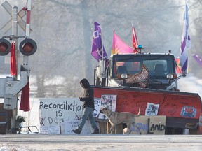 A protester walks in front of a snowplow blade that has signatures from Wet'suwet'en hereditary chiefs, at a rail blockade in Tyendinaga, near Belleville, Ont., on Feb. 21, 2020.