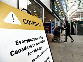 A traveller walks past signage asking international travellers to self-isolate for 14 days, at Vancouver International Aiport on March 17.