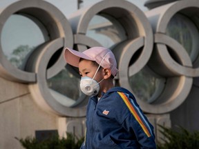 A boy wearing a face mask, amid concerns of the COVID-19 coronavirus, walks before an Olympic rings sculpture at the national 'Birds Nest' stadium, the main site of the 2008 Beijing Olympics in Beijing on March 23, 2020.