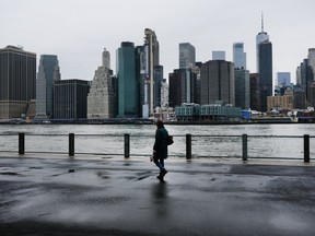 People walk in Brooklyn while lower Manhattan looms in the background on March 28, 2020 in New York City, NY. Across the country schools, businesses and places of work have either been shut down or are restricting hours of operation as health officials try to slow the spread of COVID-19.