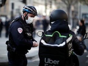 A French police officer checks a motorist in Belleville neighborhood as a lockdown imposed to slow the rate of the coronavirus disease (COVID-19) contagion started at midday in all the country, in Paris, France, March 17, 2020.