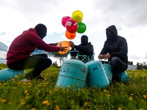 Masked Palestinians prepare to attach balloons to a gas canister before releasing it near Gaza's Bureij refugee camp, along the Israel-Gaza border fence, on February 10, 2020.