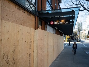 A woman walks past a Lululemon store with boarded up windows that has been closed due to the coronavirus, in Vancouver, on Wednesday, March 25, 2020.