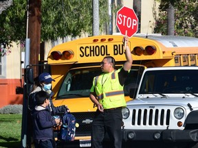 In this file photo a woman wears a facemask picking up a child as an Alhambra Unified School District as a crossing guard stops traffic outside Ramona Elementary School on February 4, 2020 in Alhambra, California.