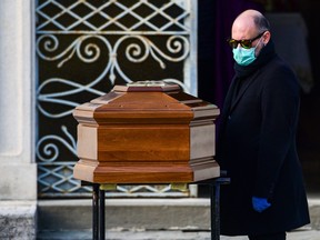 A man wearing a face mask stands by the coffin of his mother during a funeral service in the closed cemetery of Seriate, near Bergamo, Lombardy, on March 20, 2020.