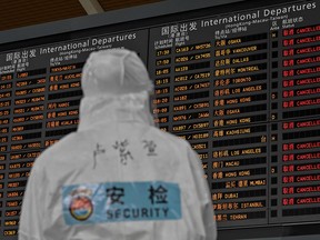 An airport security worker wearing protective gear looks at a screen showing international departures at Shanghai Pudong International Airport in Shanghai on March 19, 2020.