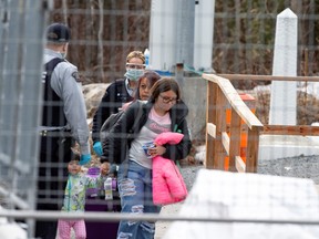 Asylum seekers cross the border from New York into Canada followed by Royal Canadian Mounted Police (RCMP) officers at Roxham Road, in Hemmingford, Quebec, Canada March 19, 2020.