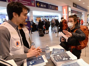 A health worker assigned by the city of Montreal greets a passenger and hands out information about COVID-19 at Montréal-Pierre Elliott Trudeau International Airport on March 16, 2020.