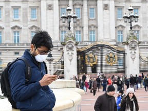 A tourist wearing a mask checks his cellphone in front of Buckingham Palace in London on March 14, 2020.