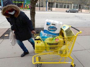 A woman wears a face mask as she pulls her grocery cart March 14, 2020 to her Palace Centre apartment on State Street in Erie, Pa.