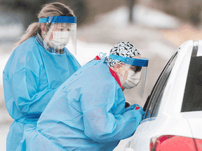 Healthcare workers talk to a driver before issuing a test at a drive-thru COVID-19 evaluation clinic in Montreal, March 29, 2020.