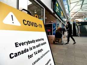 A woman walks past signage asking international travellers to self-isolate for 14 days in Vancouver International Aiport on March 17, 2020.