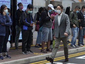 People wearing face masks to protect against the coronavirus walk along a street in Hong Kong Tuesday, March 17, 2020.