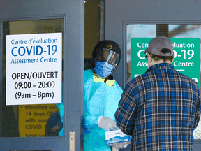 A staff member provides a face mask to a man before he enters the COVID-19 Assessment Centre in Ottawa.