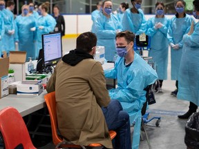 A health care worker speaks to a test patient, a staff member portraying the role of a patient to ensure the assessment systems are working, at an assessment table as they prepare for the opening of the COVID-19 Assessment Centre at Brewer Park Arena in Ottawa, during a media tour on Friday, March 13, 2020.