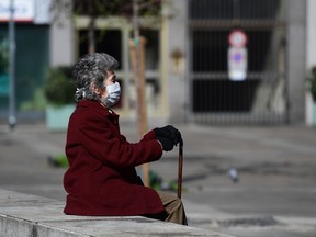 In this file photo taken on March 8, 2020, an elderly woman wearing a protective face mask sits on a bench in the city centre of Milan, after millions of people were placed under forced quarantine in northern Italy.
