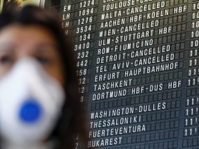 Travellers wear face masks near a flight departure information board showing a cancelled flight to Detroit at Frankfurt Airport, operated by Fraport AG, in Frankfurt, Germany, March 12, 2020.