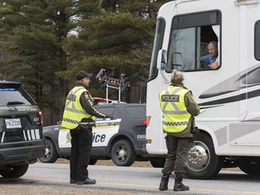 Members of Quebec's provincial police force talk to the driver of a recreational vehicle near the border of the United States in Saint-Bernard-de-Lacolle, south of Montreal, Saturday, March 28, 2020, as Coronavirus COVID-19 cases rise in Canada and around the world.
