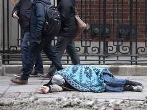 A homeless person lies on the sidewalk in the heart of Toronto's financial district on a cold winter's day, on Jan. 23, 2020.