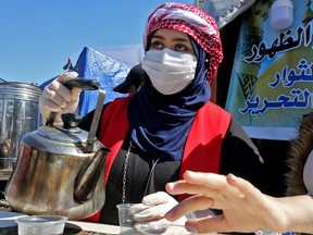 An Iraqi woman wearing a protective mask amid fears of the spread of the coronavirus serves tea on March 4, 2020 in Baghdad's Tahrir square where anti-government protesters continue their sit-in since last October. - Iraq reported its first coronavirus case last week in the southern shrine city of Najaf, which has sparked public panic in the country, one of Iran's largest export markets and a popular destination for Iranian Shiite Muslim pilgrims.