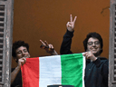Men hold an Italian flag as they look out of an apartment window as part of a flashmob organized to raise morale during Italy's coronavirus crisis in Rome, March 13, 2020.