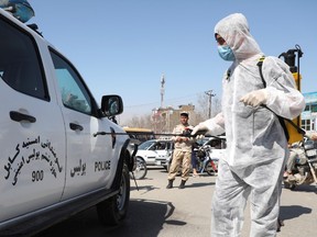 A member of civil society activist in a protective suit sprays a disinfectant over a police vehicle during a campaign awareness of the coronavirus in Kabul, Afghanistan March 18, 2020.