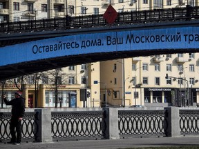 A person takes a picture with a photo in front of a bridge bearing the words 'Stay Home. Your Moscow Metro' downtown Moscow in downtown Moscow on March 29, 2020, as the city attempts to curb the spread of the COVID-19 (novel coronavirus).