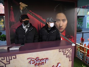 This photo taken on February 16, 2020 shows two workers wearing face masks manning a promotional stand for the Disney move "Mulan" in an almost empty shopping mall in Beijing.