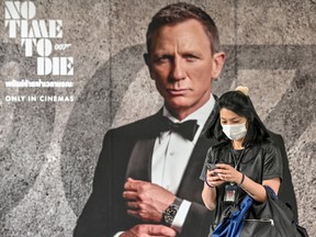 In this file photo taken on February 28, 2020, a woman wearing a facemask amid fears of the spread of the COVID-19 novel coronavirus walks past a poster for the new James Bond movie "No Time to Die" in Bangkok.