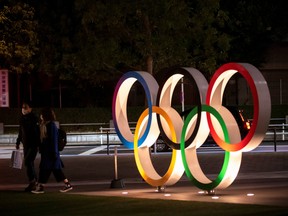 A couple wearing protective face masks, following the outbreak of the coronavirus, walk past The Olympic rings in front of the Japan Olympics Museum in Tokyo, Japan, March 3, 2020.