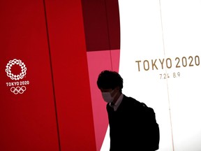 A man wearing a protective face mask, following an outbreak of the coronavirus disease (COVID-19), walks past the upcoming Tokyo 2020 Olympics decoration board in Tokyo, Japan, March 23, 2020.