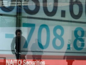 People are reflected in a window showing a drop in share price numbers of the Tokyo Stock Exchange in Tokyo on March 30, 2020. Tokyo stocks opened down more than three per cent today.